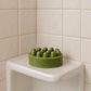 Green Good Hair Day shampoo bar with raised massage bumps on a white corner shower shelf.
