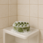 Green Good Hair Day shampoo bar covered in white lather on a corner shower shelf.
