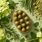 Oval Good Hair Day shampoo bar with raised massage bumps, surrounded by rosemary, mint leaves, flowers and green powder.
