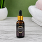 Bottle of beard growth oil with dropper on a wooden surface with towels and plants in the background