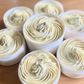 Open white tubs filled with pale whipped hair and body butter piped into swirls on a wooden surface.
