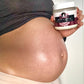 Person holding a Naiga Naturals Cocoa & Vanilla Whipped Hair and Body Butter tub beside their bare pregnant belly.
