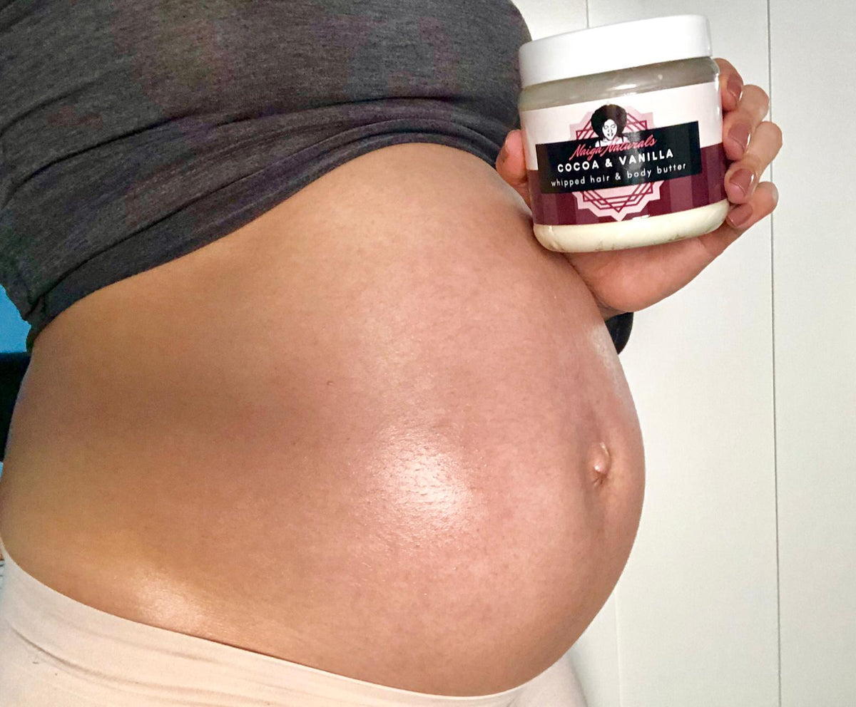 Person holding a Naiga Naturals Cocoa & Vanilla Whipped Hair and Body Butter tub beside their bare pregnant belly.
