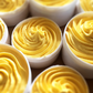 Open white tubs of yellow Mango Twist whipped hair and body butter piped into swirls.
