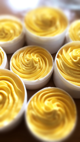 Open white tubs of yellow Mango Twist whipped hair and body butter piped into swirls.
