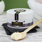 Naiga Naturals Pure Shea Nilotica butter jar on black slate beside a wooden spoon holding pale shea butter.
